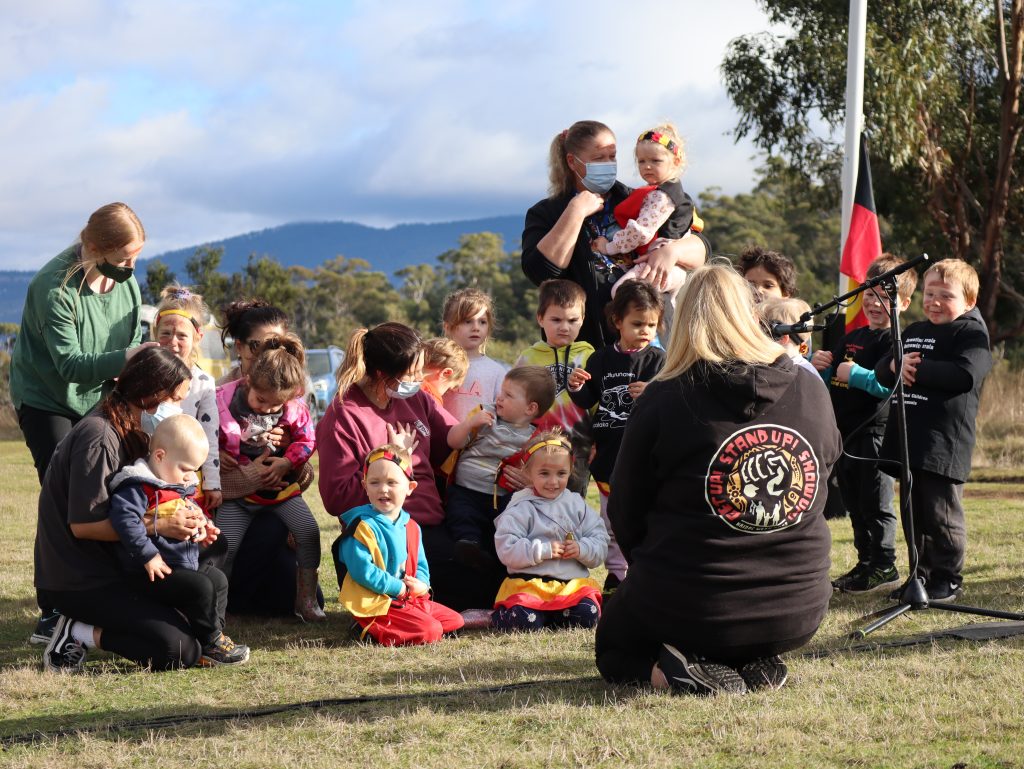 A group of small Aboriginal chidren sitting in a group as they sing during NAIDOC Week Flag Raising 2022